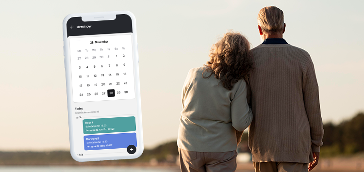 A phone showing a MiniFinder Live app in the calendar view and notifications for medication. An elderly couple in walking in the sunset in the background.