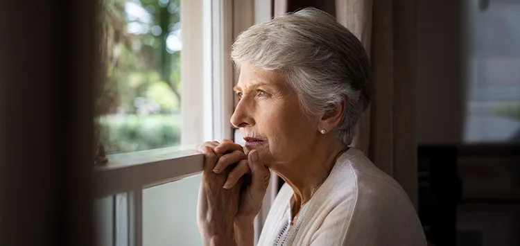 Ältere Person sitzt zu Hause mit einem Hausnotruf für mehr Sicherheit und Nähe bei Einsamkeit.