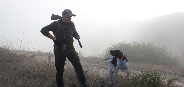 Hunter following a hunting dog during an active hunt in natural terrain