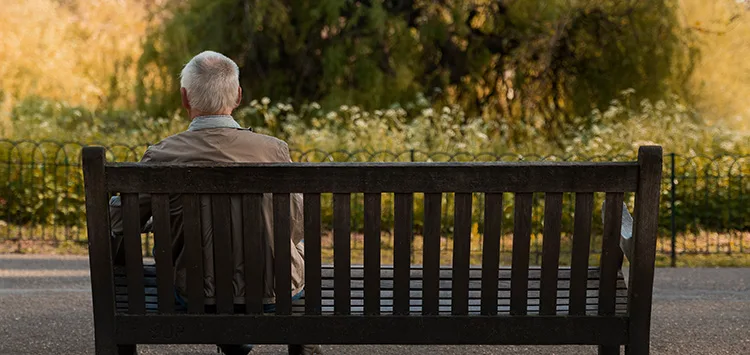 Äldre man med demens sitter hemma och tittar lugnt ut genom fönstret.
