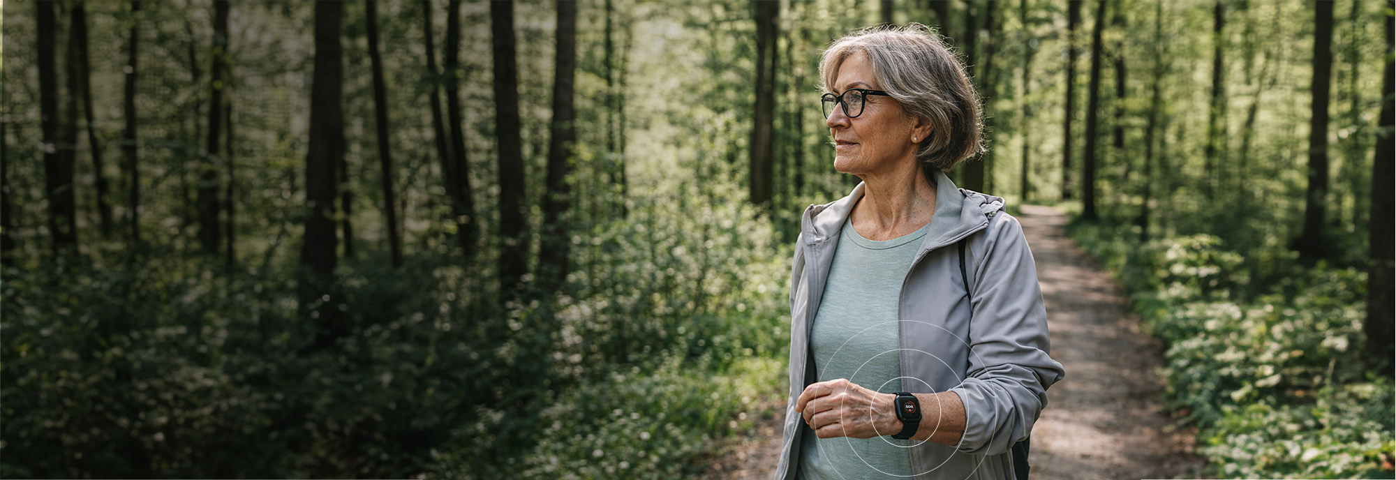 Äldre kvinna promenerar i skogen med MiniFinder Watch på handleden och känner trygghet genom sitt mobila trygghetslarm.