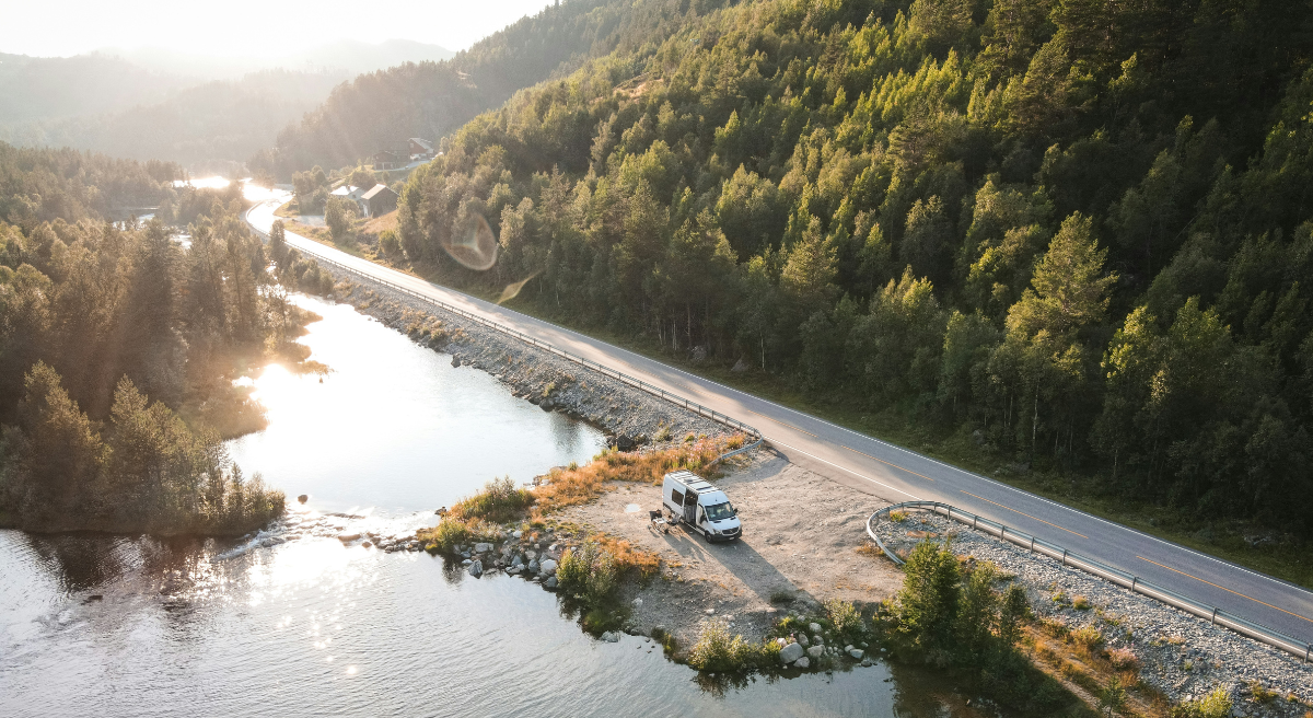 Autocamper parkeret ved en sø langs en snoet landevej omgivet af skov og bjerge