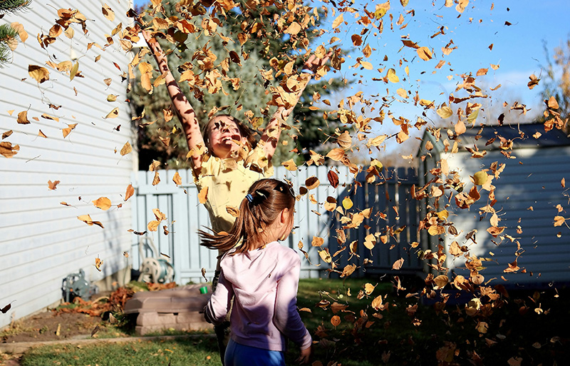 Två barn med MiniFinder Kids Watch på handleden kastar höstlöv i luften.